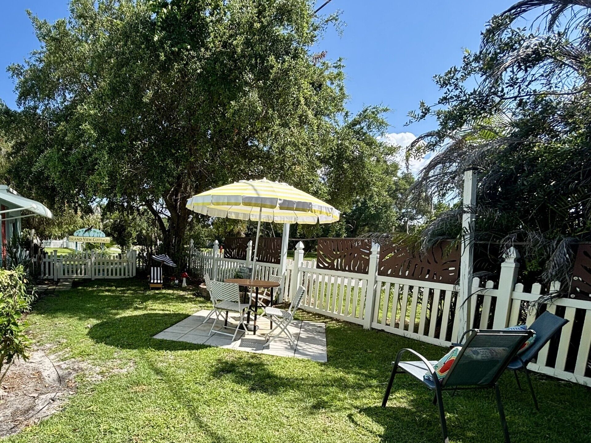 A backyard with a white picket fence, a table with chairs, and a yellow umbrella.