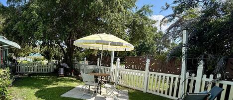 A backyard with a white picket fence, a table with chairs, and a yellow umbrella.