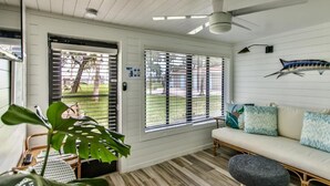 Una habitación con ventilador de techo, sofá, mesa de comedor y un amplio ventanal con persianas.