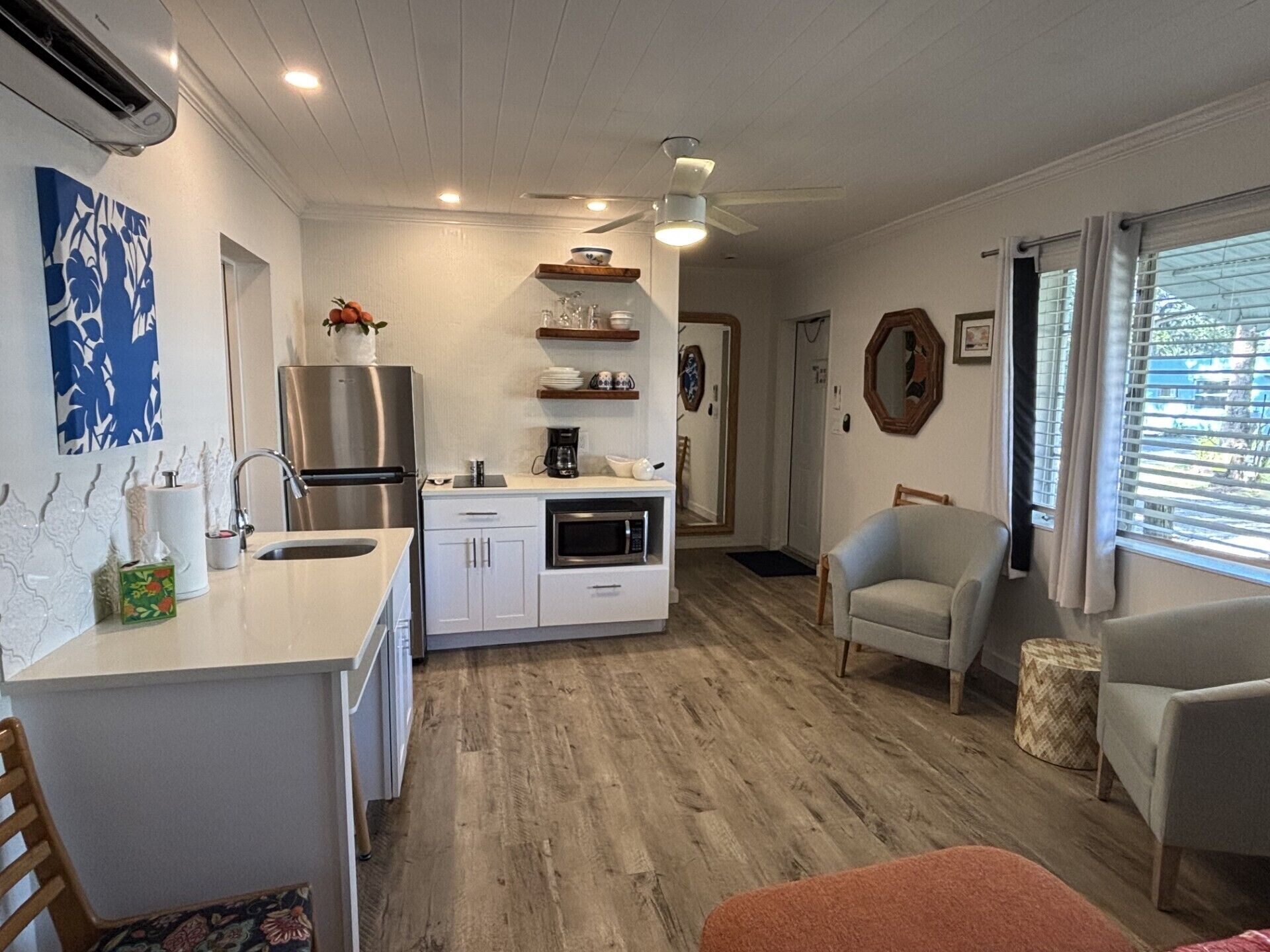 A compact kitchen with a refrigerator, microwave, and coffee maker. There is a dining area with a chair and a small table.