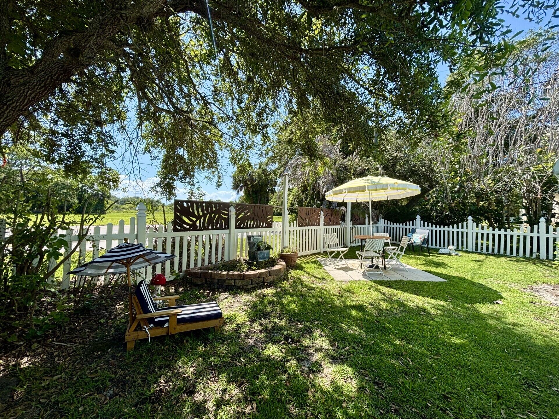 A backyard with a wooden deck, a white picket fence, and a patio area with a table and chairs.