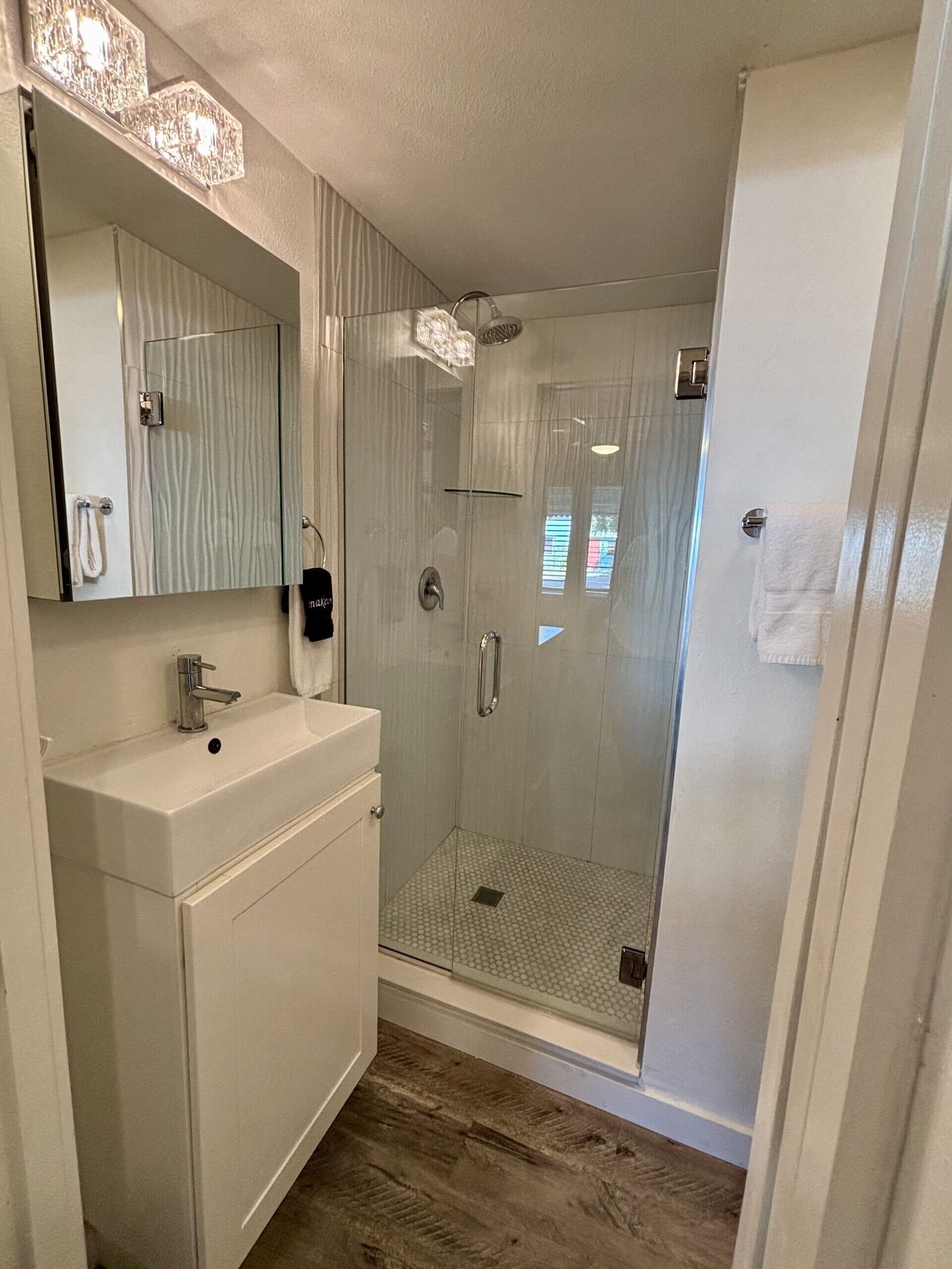 Une salle de bain avec une douche à parois de verre, un lavabo avec un miroir et un porte-serviettes.
