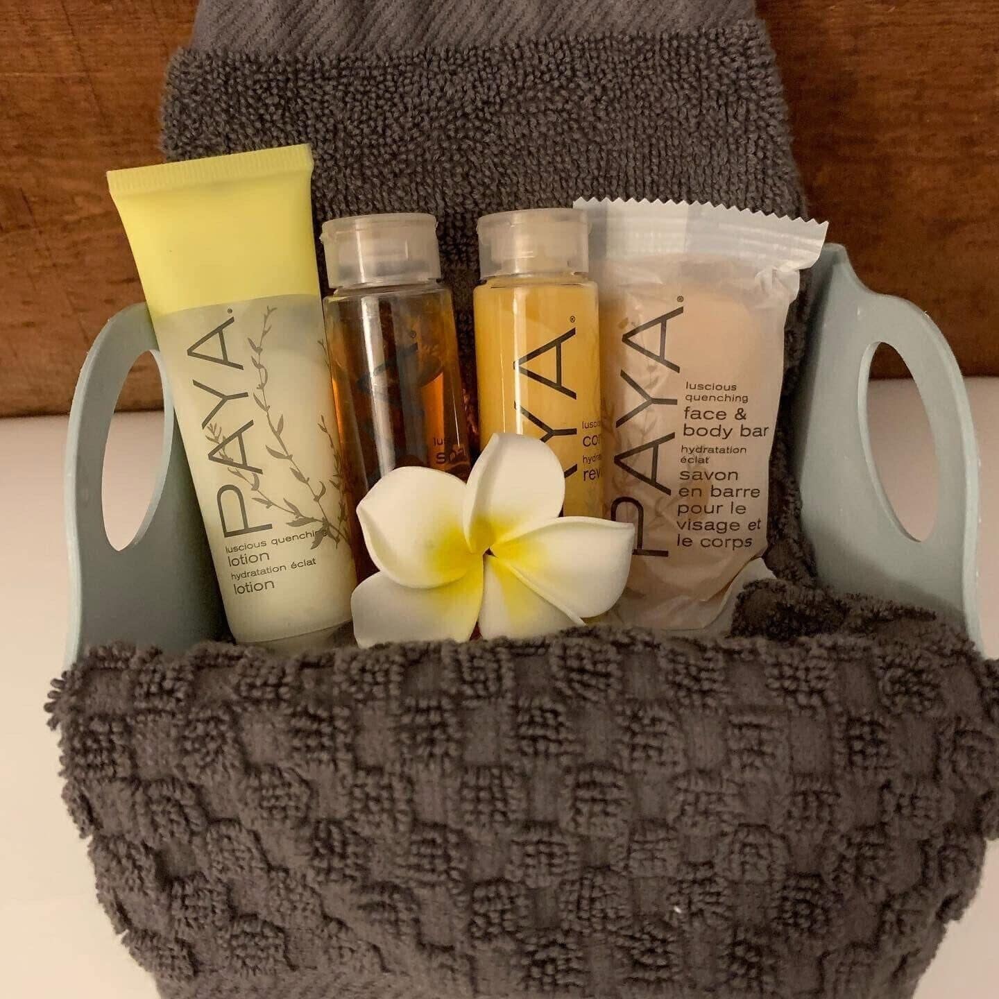 A gray woven basket containing four bottles of Paya skincare products, a white flower, and a gray towel.