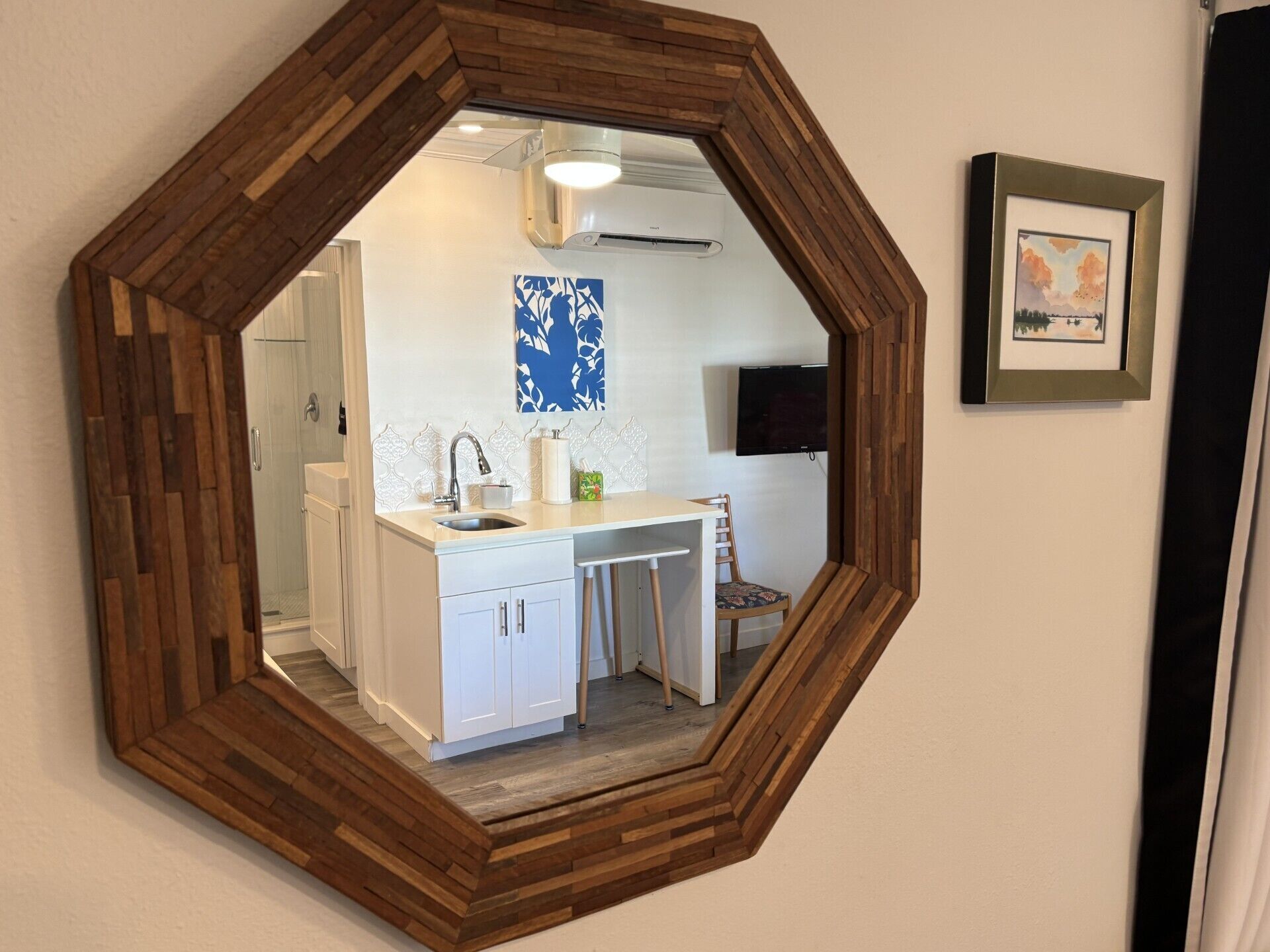 Un miroir hexagonal avec un cadre en bois, une cuisine avec des meubles blancs, un évier et une chaise.