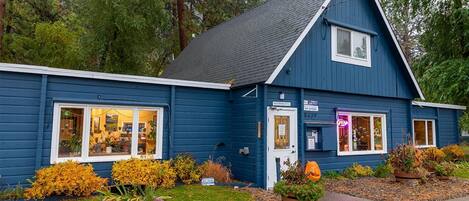 A blue building with a sloped roof, a front entrance, and a window displaying items.
