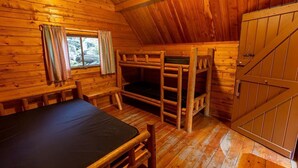 Uma cabana de madeira com beliches, uma mesa e uma janela com cortinas.