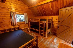 Una cabaña de madera con literas, una mesa y un ventanal con cortinas.