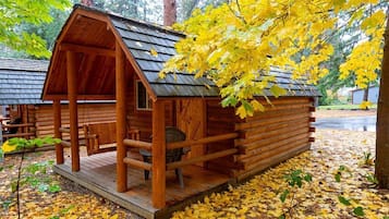 A wooden cabin with a porch, surrounded by autumn foliage.