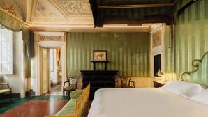 A hotel room with a large bed, a wooden dresser, a framed picture on the wall, and a green upholstered chair. - Guelfa 19 - (2) - One Bedroom Apartment, Sleeps 2 (Cortona)