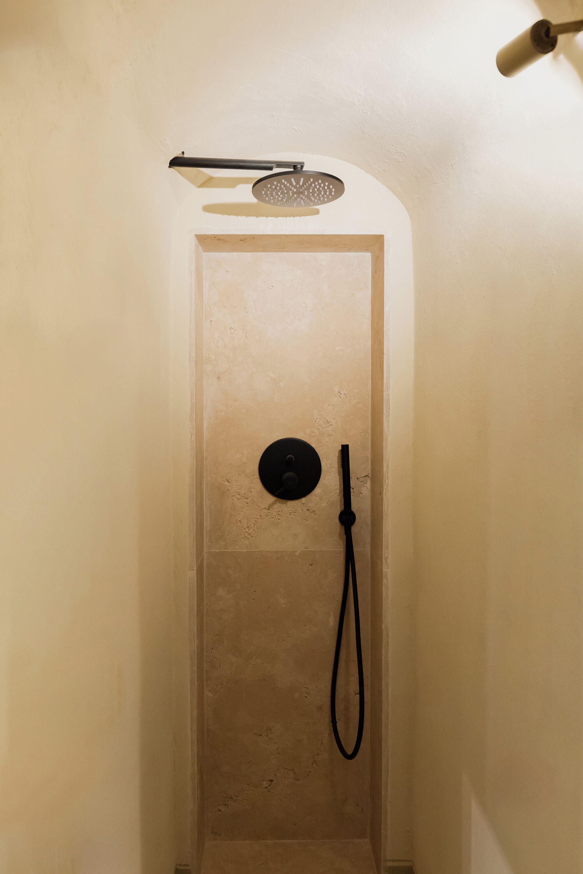 Un espacio de ducha estrecho con un cabezal de ducha manual y un cabezal de ducha circular montado en la pared.
