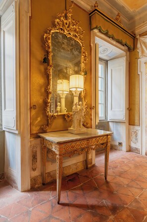 A room with a large ornate mirror, a table with a lamp, and a door leading to another room. - Guelfa 19 - (1) - Two Bedroom Apartment, Sleeps 4 (Cortona)