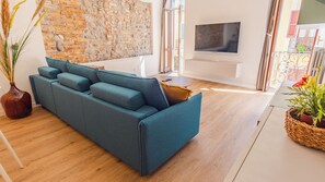 A modern living room with a blue sofa, a stone wall, a TV, and a balcony with plants. - La Piazzuola - One Bedroom Apartment, Sleeps 4 (Salo)