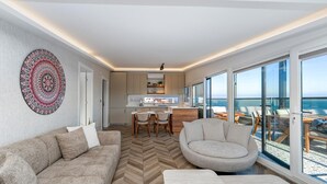 A modern living room with a herringbone floor, a sofa, a round armchair, and a dining area with a kitchen in the background.
