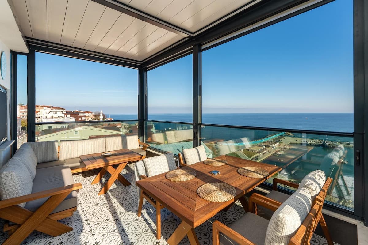 Un balcón con vista al mar, una mesa de madera y un sofá.