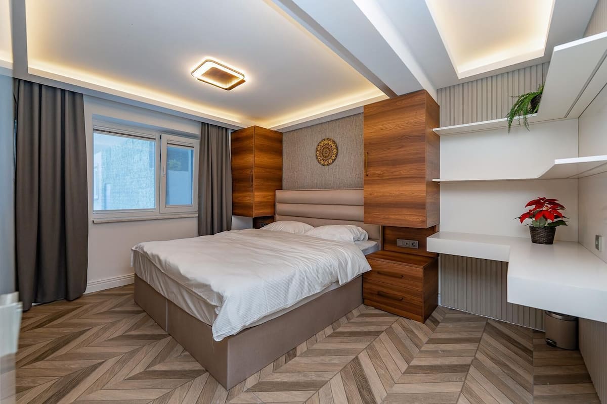 Un dormitorio moderno con cama, estanterías empotradas, un adorno en la pared y una ventana con cortinas.