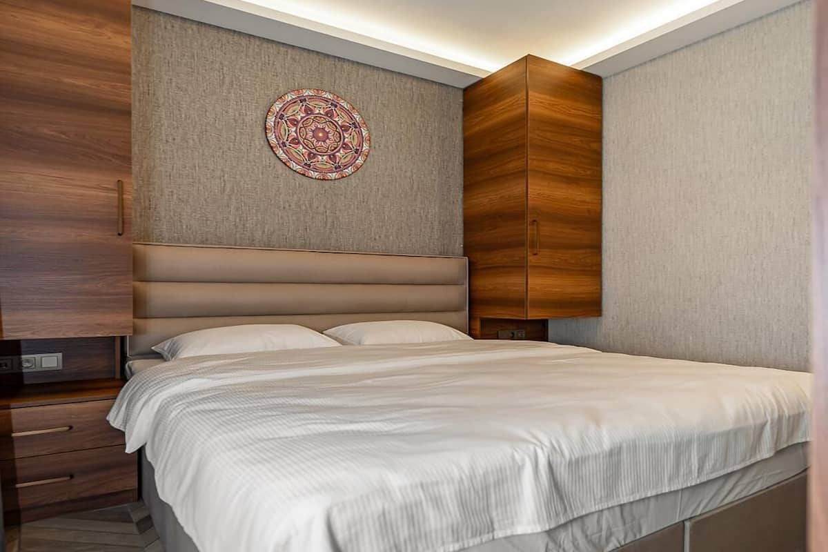 Un dormitorio moderno con cama, armarios de madera, una lámpara de pared y decoración mural estampada.