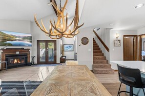 Un intérieur moderne avec une grande table à manger, une cheminée, un escalier et une vue sur un paysage naturel.