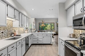 Une cuisine moderne avec des meubles blancs, un îlot central et une grande fenêtre offrant une vue sur l’extérieur.
