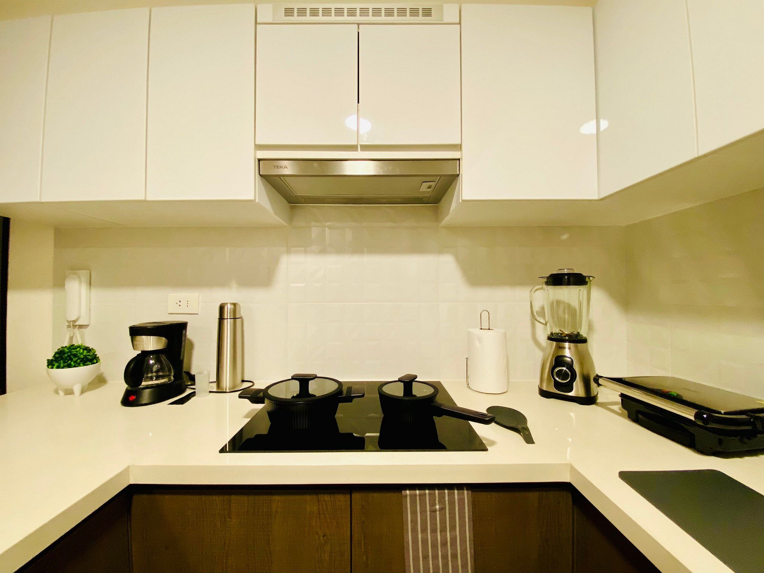 Una cucina moderna con mobili bianchi, una cappa aspirante in acciaio inossidabile, una macchina da caffè, un frullatore e un bollitore.