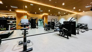 Ein Fitnessraum mit unterschiedlichen Trainingsgeräten, einer Spiegelwand und einer Holzboden.