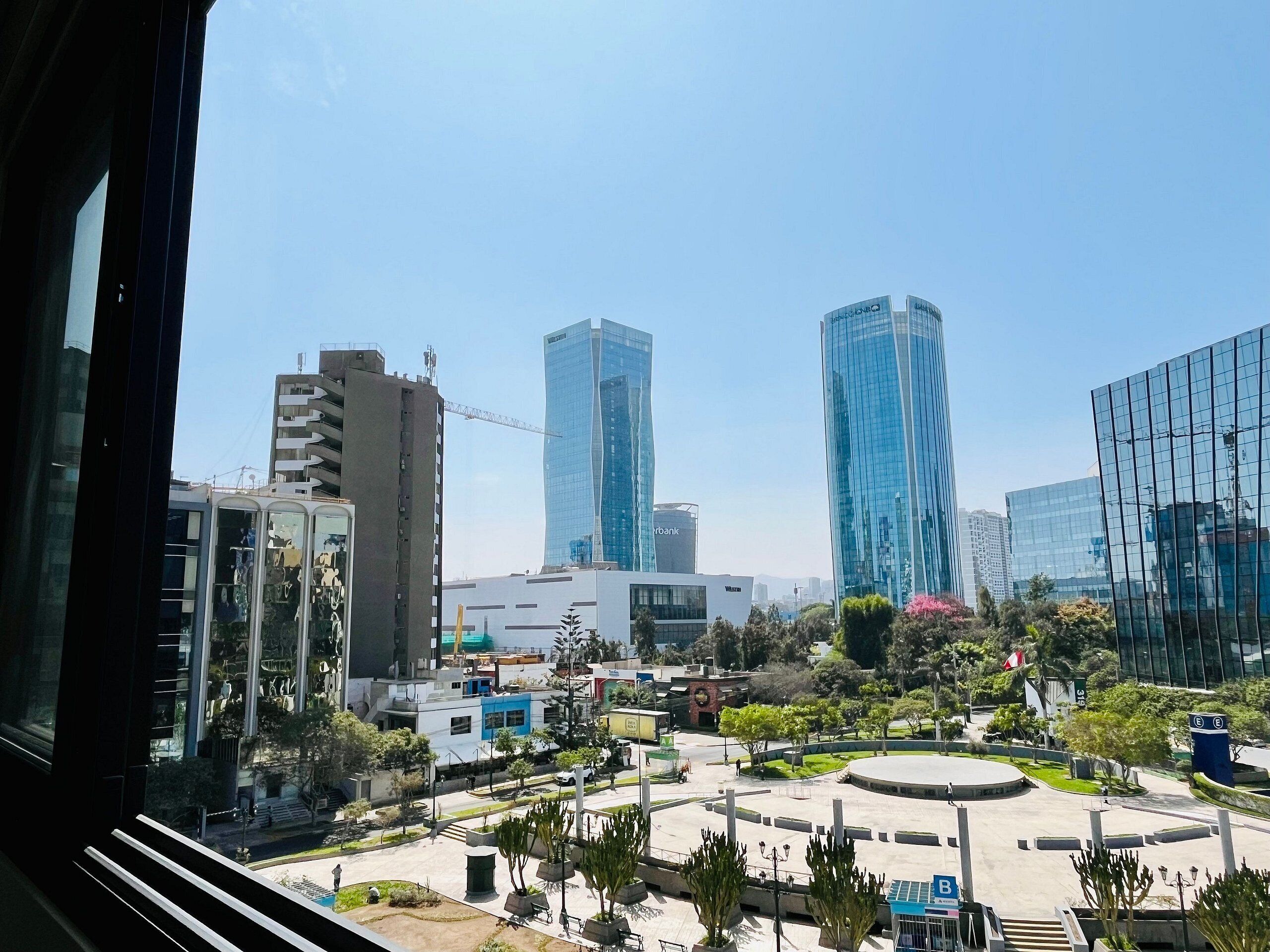 A cityscape with modern buildings, a central plaza with a circular design, and a few trees.
