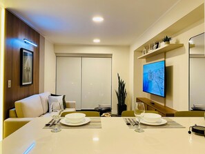 A modern dining area with a table set for two, a television mounted on the wall, and a sliding door closet. - Executive Apart en San Isidro WiFi Pool (Lima)
