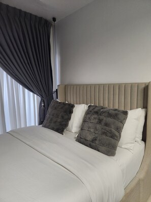 A bed with a beige headboard, two pillows, and a white bedspread. - A perfect cosy studio in Eastlegon Accra with a pool,restaurant and fitness room (Accra)