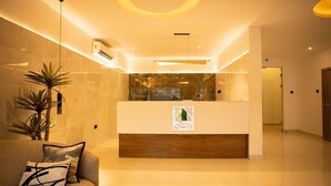Un área de recepción con un mostrador de madera, una planta en maceta y un sofá con cojín.