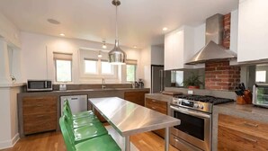 A modern kitchen with a central island, stainless steel appliances, and wooden cabinetry. - The Modern Cottage Bend (Bend)