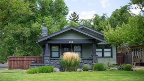A single-story house with a stone foundation, a green roof, and a number '256' displayed on the front. - The Modern Cottage Bend (Bend)
