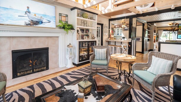 A spacious living room with a fireplace, wicker furniture, and a large painting of a boat on the wall. - Private Pickleball Court + Riverfront Bend Retreat (Bend)