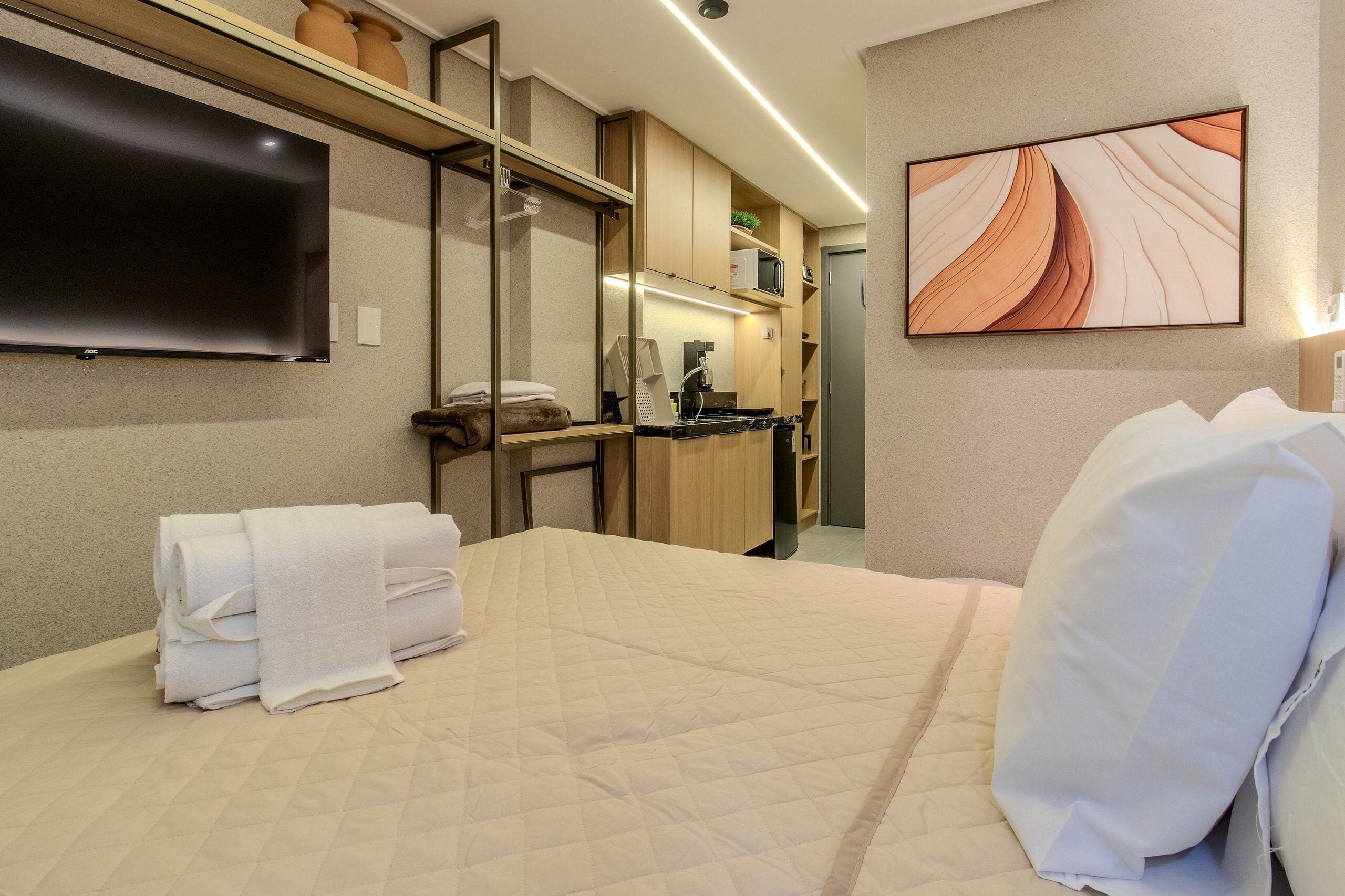 Habitación de hotel con cama, televisor de pantalla plana, microondas, lavamanos y un cuadro en la pared.