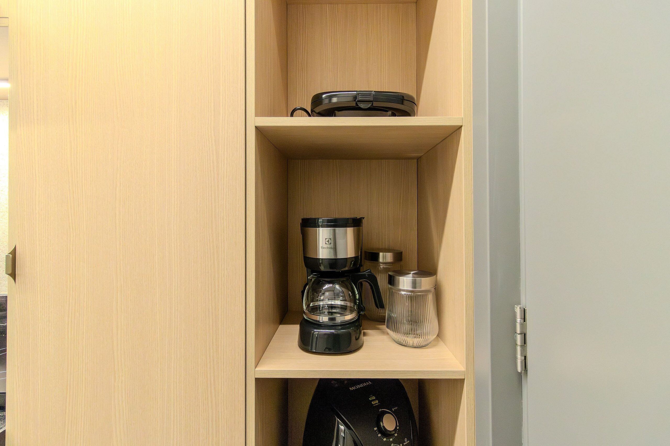 A wooden cabinet with a coffee maker, a glass carafe, and a thermos on the shelf.