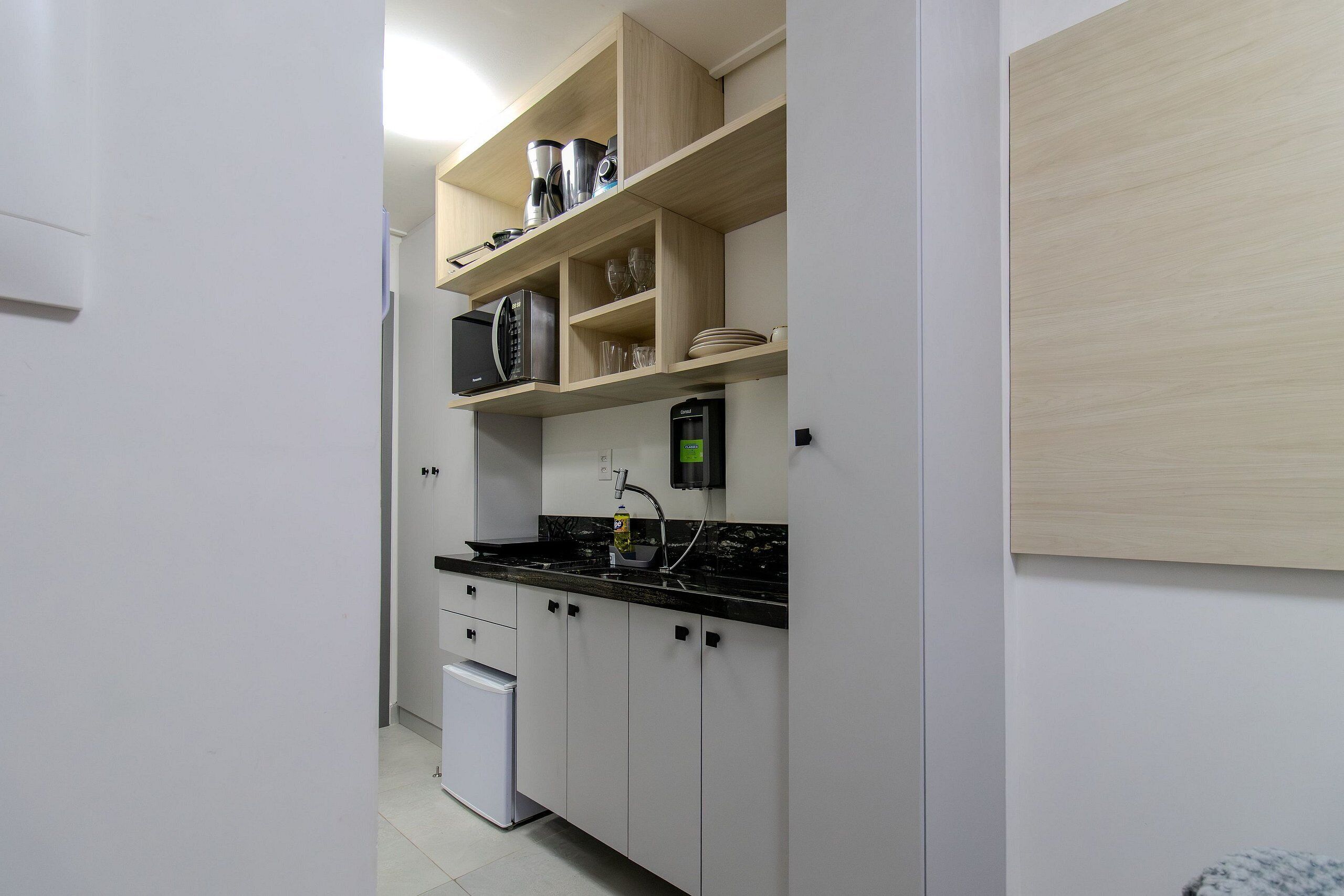 Una cucina compatta con frigorifero, forno a microonde e macchina da caffè sul piano di lavoro.