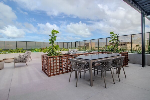 Une terrasse sur le toit avec une table et des chaises, un fauteuil en osier et des plantes en pot.