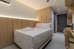 Ett modernt hotellrum med en säng, sängbord, ett inbyggt skrivbord och en duschhörna.