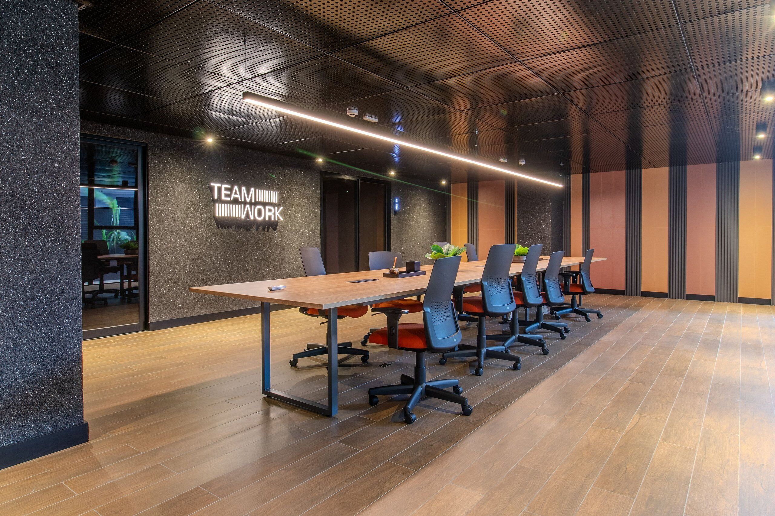 A conference room with a long table, multiple chairs, and a 'TEAMWORK' sign on the wall.