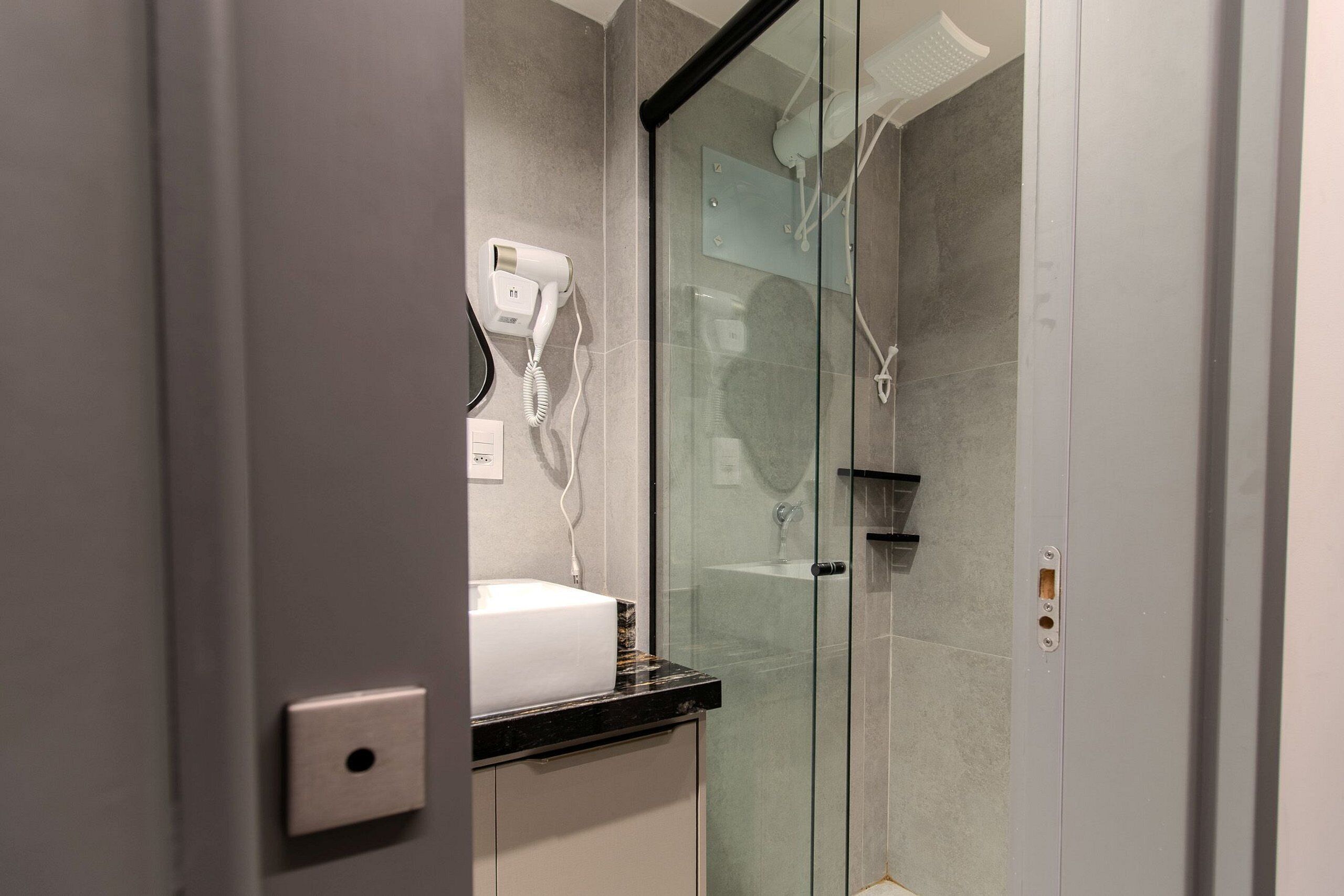 Une salle de bain avec une douche à parois de verre, un sèche-cheveux fixé au mur et un lavabo.