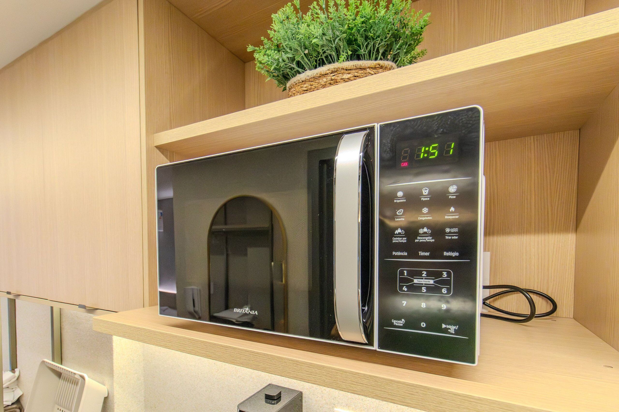 A modern kitchen with a built-in microwave, a digital clock, and a small potted plant on the shelf.