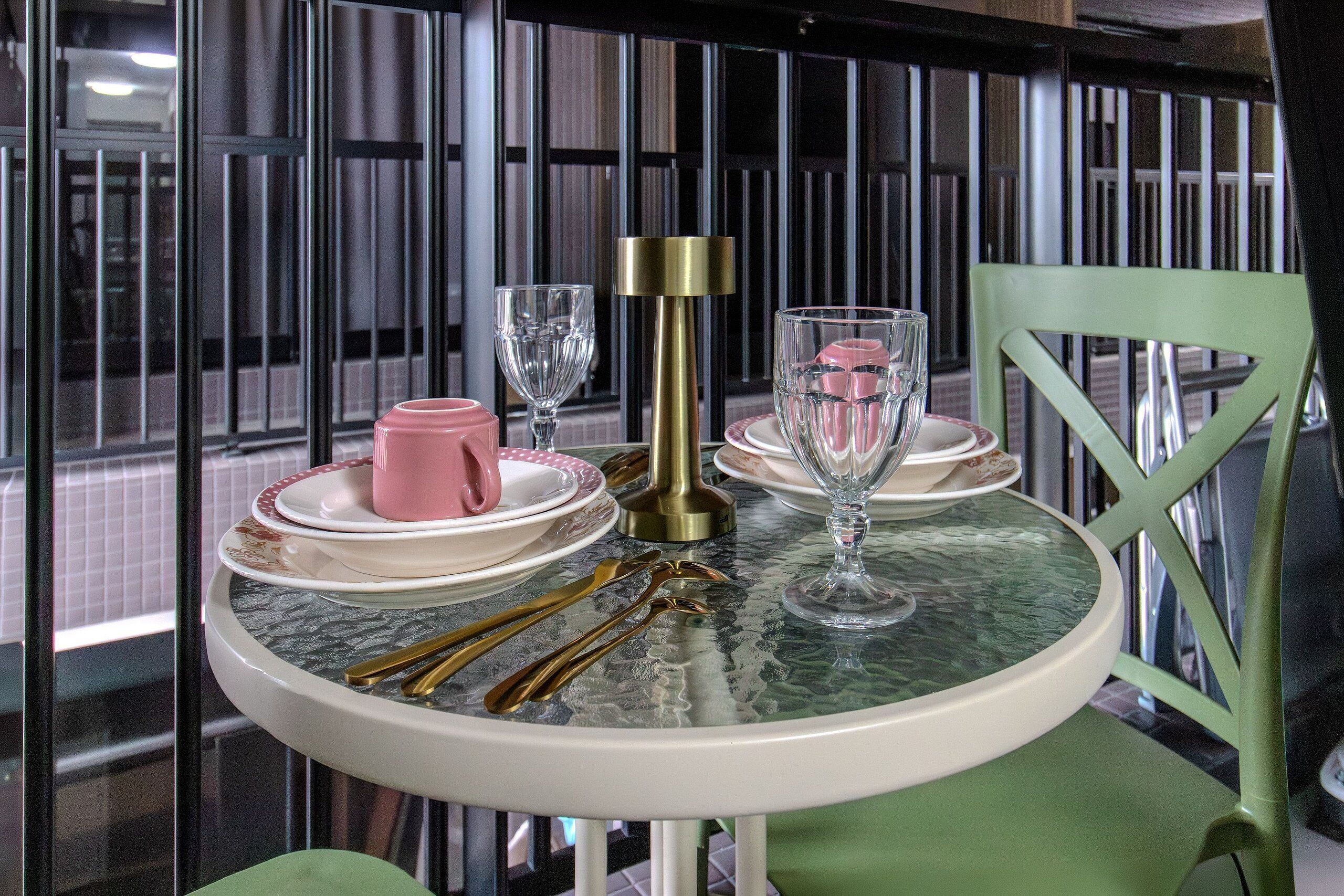 Una mesa de comedor con superficie de vidrio, rodeada de sillas, y vista a un edificio a través de una ventana.