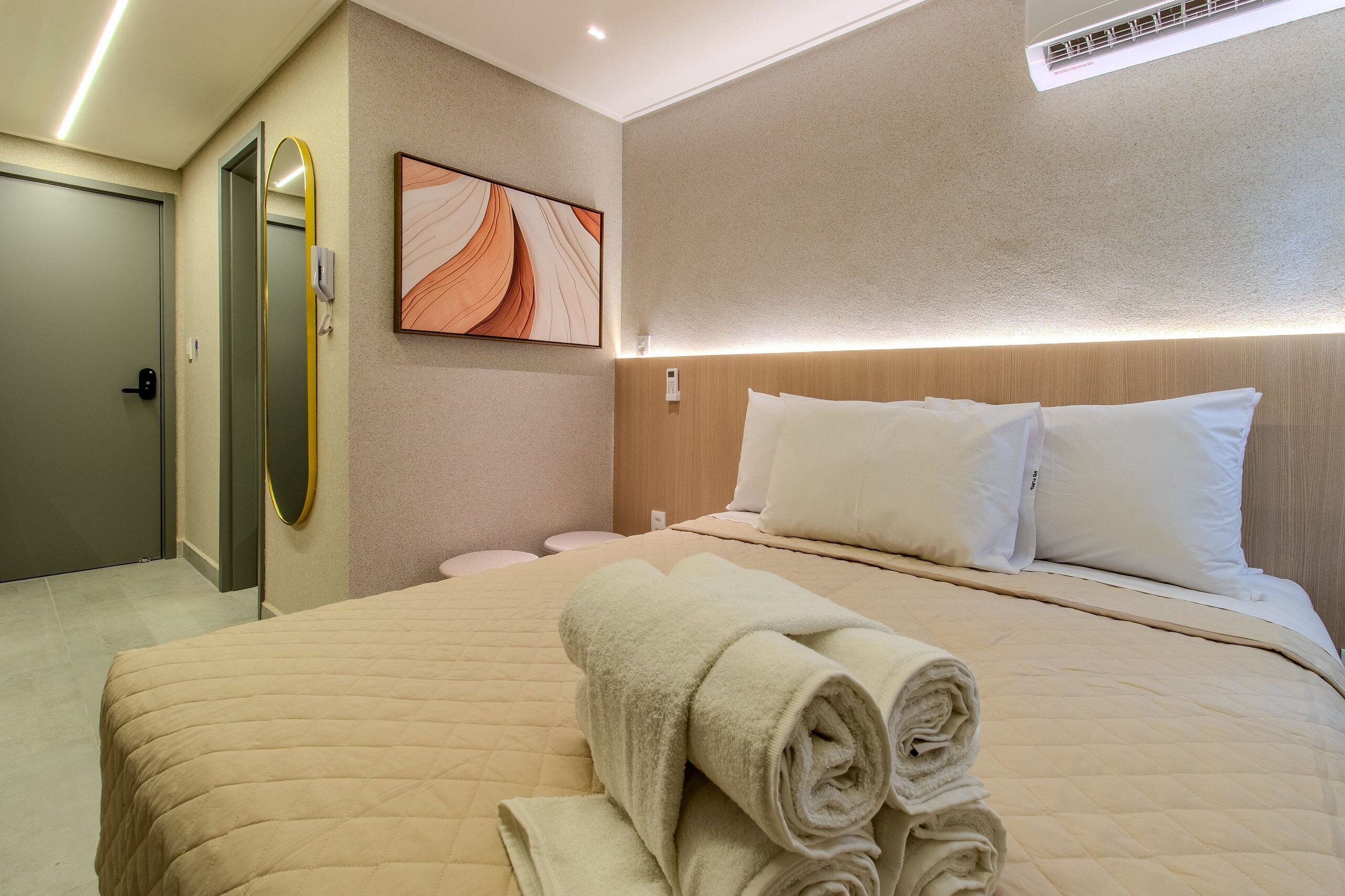 Une chambre d’hôtel avec un lit, un miroir fixé au mur, un tableau et un lit parfaitement fait, avec des serviettes pliées.