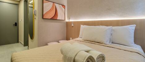 Une chambre d’hôtel avec un lit, un miroir fixé au mur, un tableau et un lit parfaitement fait, avec des serviettes pliées.