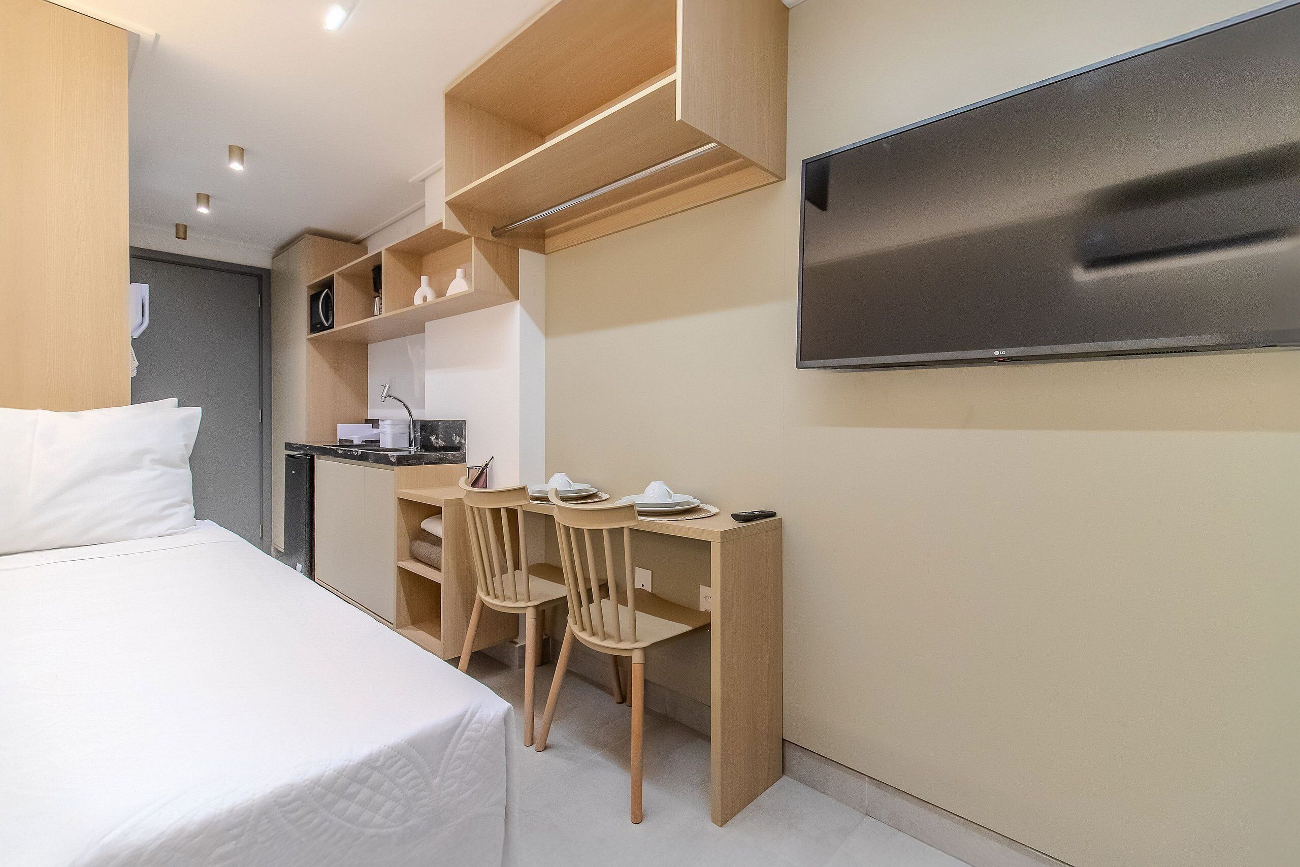 A hotel room with a bed, a desk with chairs, a flat-screen TV, and built-in shelves.