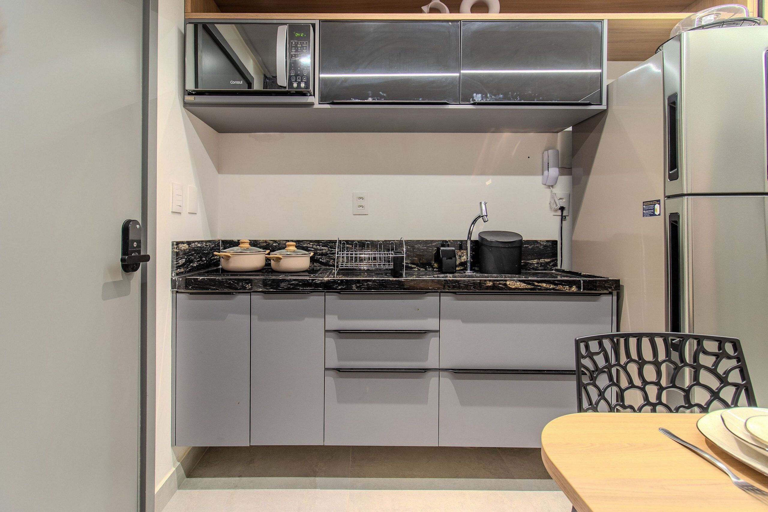 A compact kitchen with a microwave, stove, and refrigerator. There is a dining table with chairs.