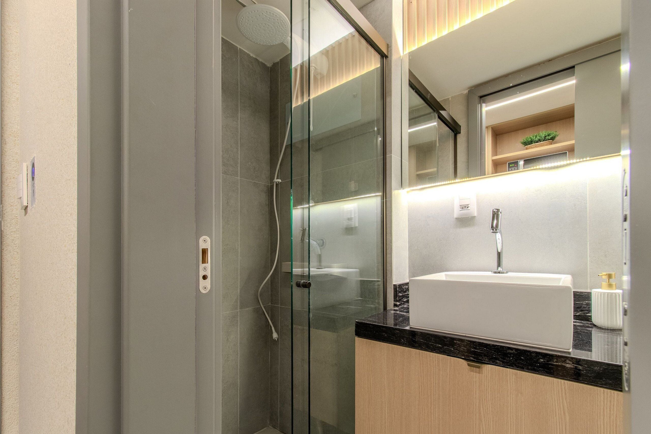 A modern bathroom with a glass shower enclosure, a white sink, and a wooden vanity.