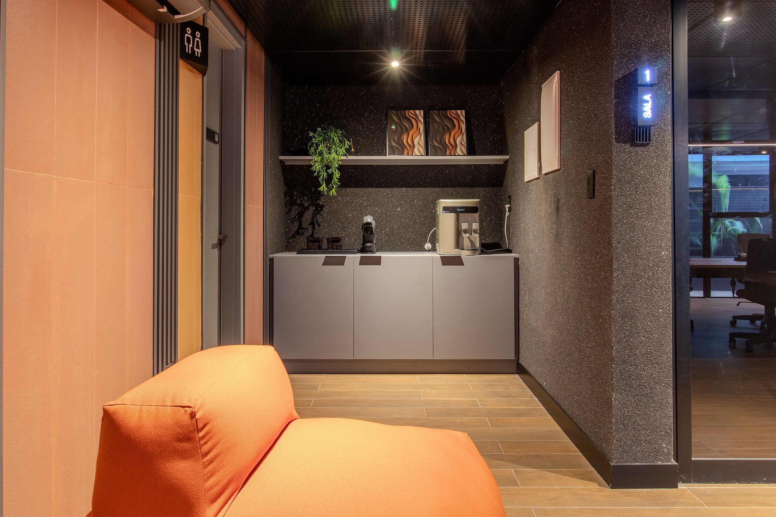 A modern hotel lobby with a reception desk, a seating area, and a view into the office space.