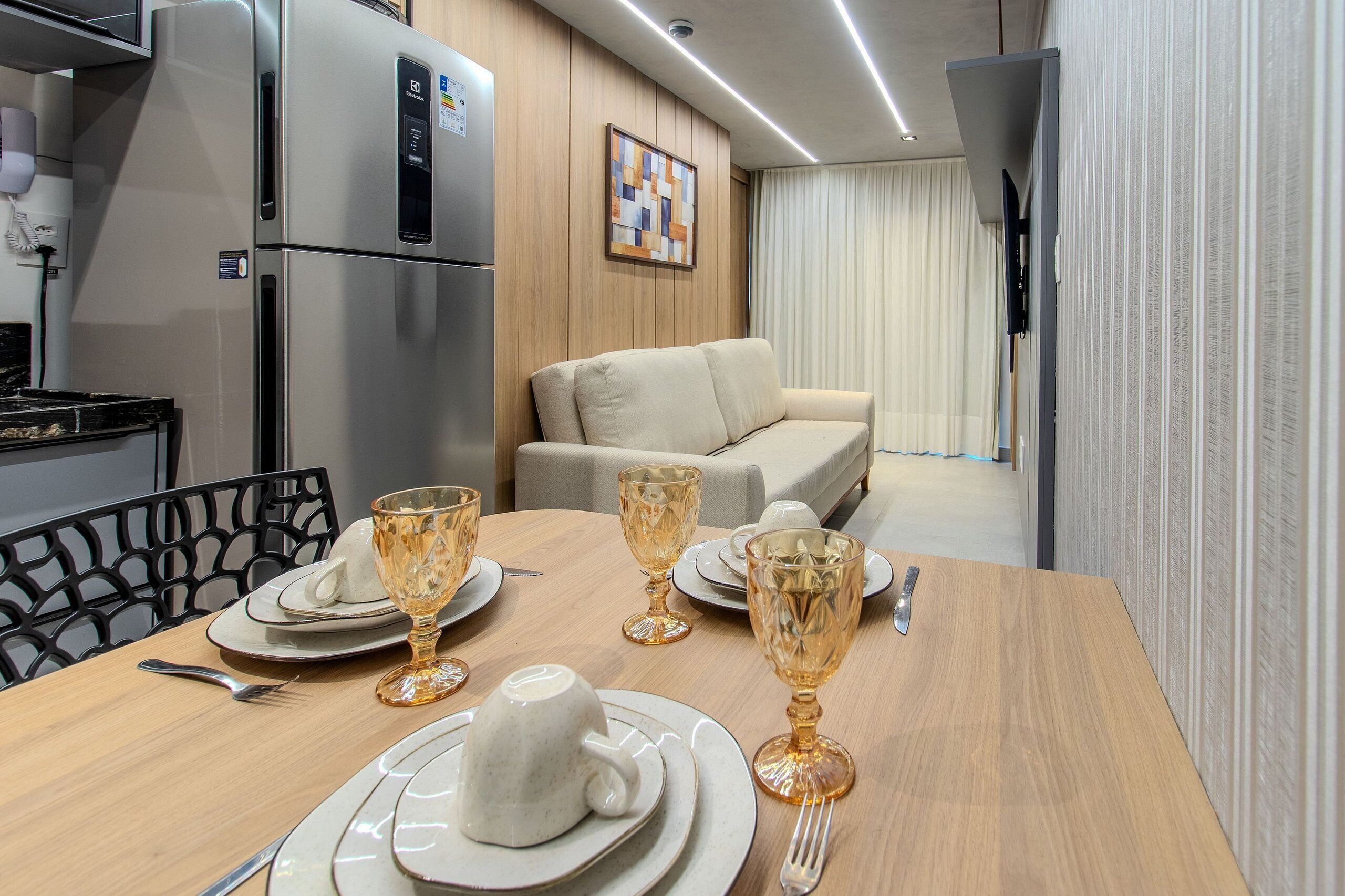 Un comedor con una mesa preparada para cuatro personas, un sofá, un refrigerador y un teléfono instalado en la pared.