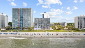 Un hotel frente a la playa con varios edificios altos, una playa de arena y sombrillas.