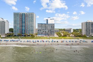 Ein Strandhotel mit mehreren Hochhäusern, einem Sandstrand und Sonnenschirmen.
