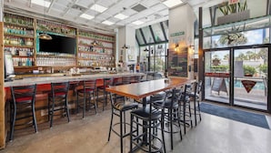 Un bar con una barra alargada, varios taburetes y una gran variedad de botellas y vasos en estantes.